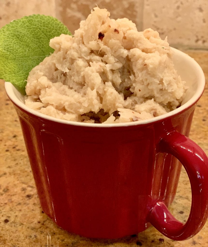 bowl with handle full of mashed cauliflower garnished with a green leaf.