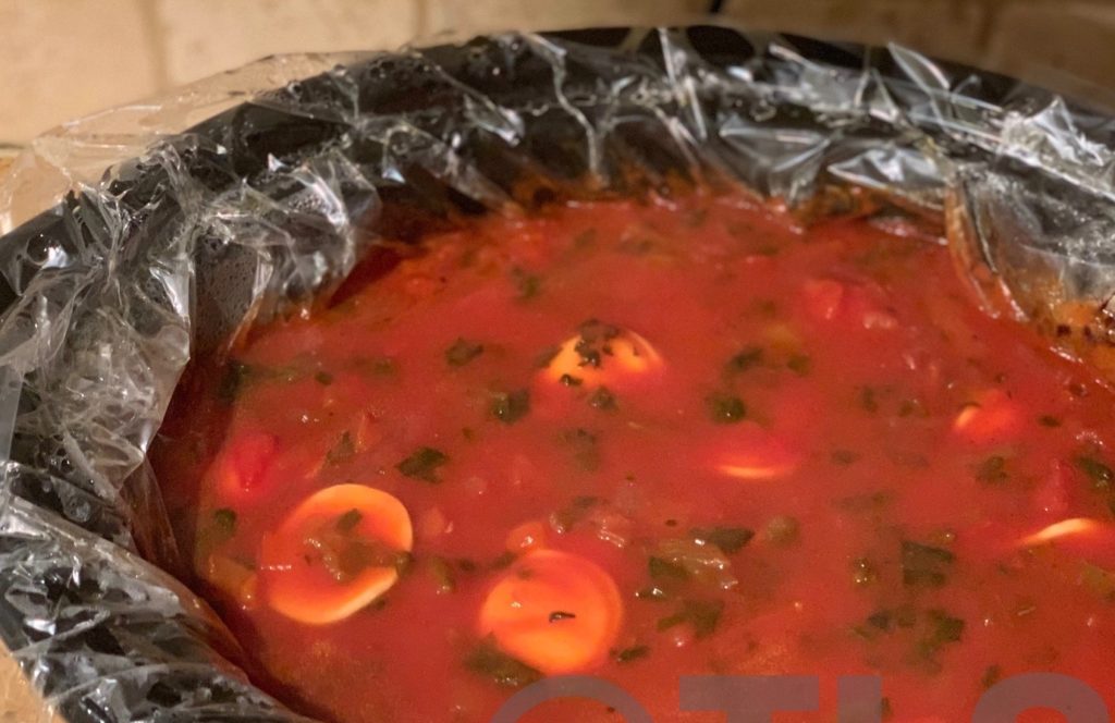 Slow cooker pot filled with warm, thick red soup base and ravioli pillows
