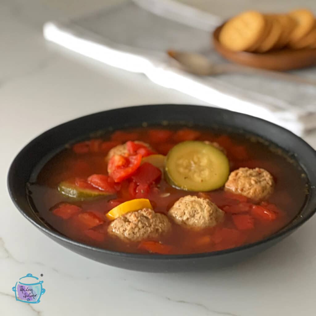 A bowl of turkey meatball soup with crackers in the background