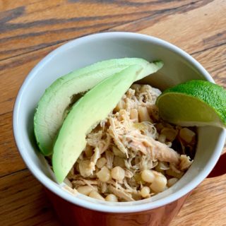 chicken and corn chili with avocado slices and a lime wedge in a red cup