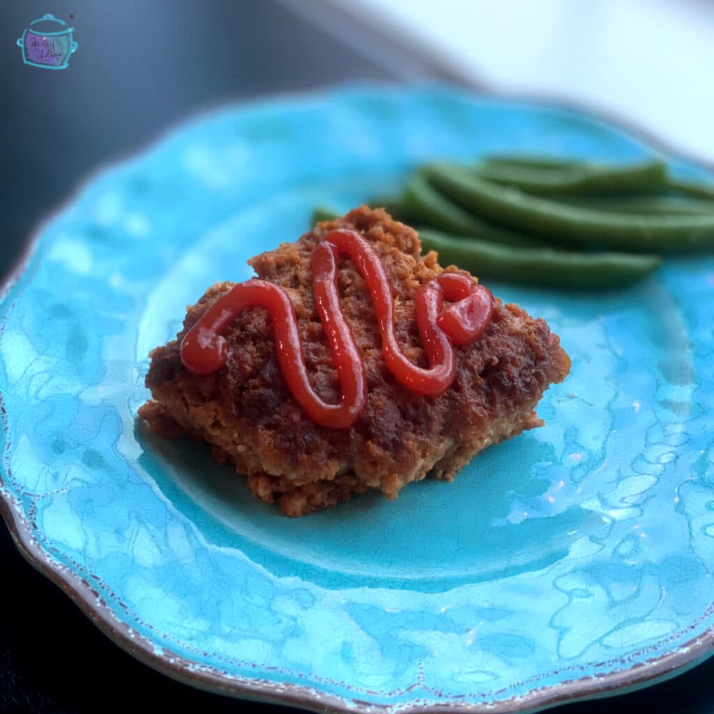 Square piece of slow cooker meatloaf topped with sauce and green beans in the background