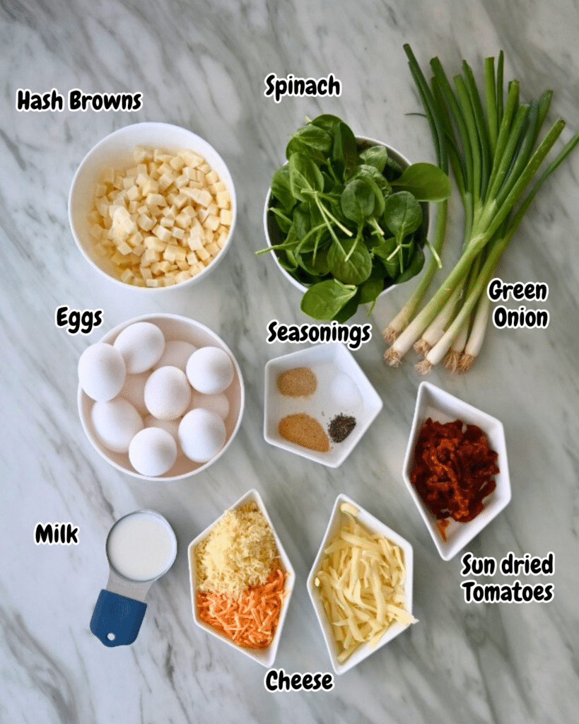 A top-down view of ingredients on a marble surface: diced hash browns, fresh spinach, green onions, eggs, milk, three seasonings, shredded cheese, and sun-dried tomatoes, each labeled with text.
