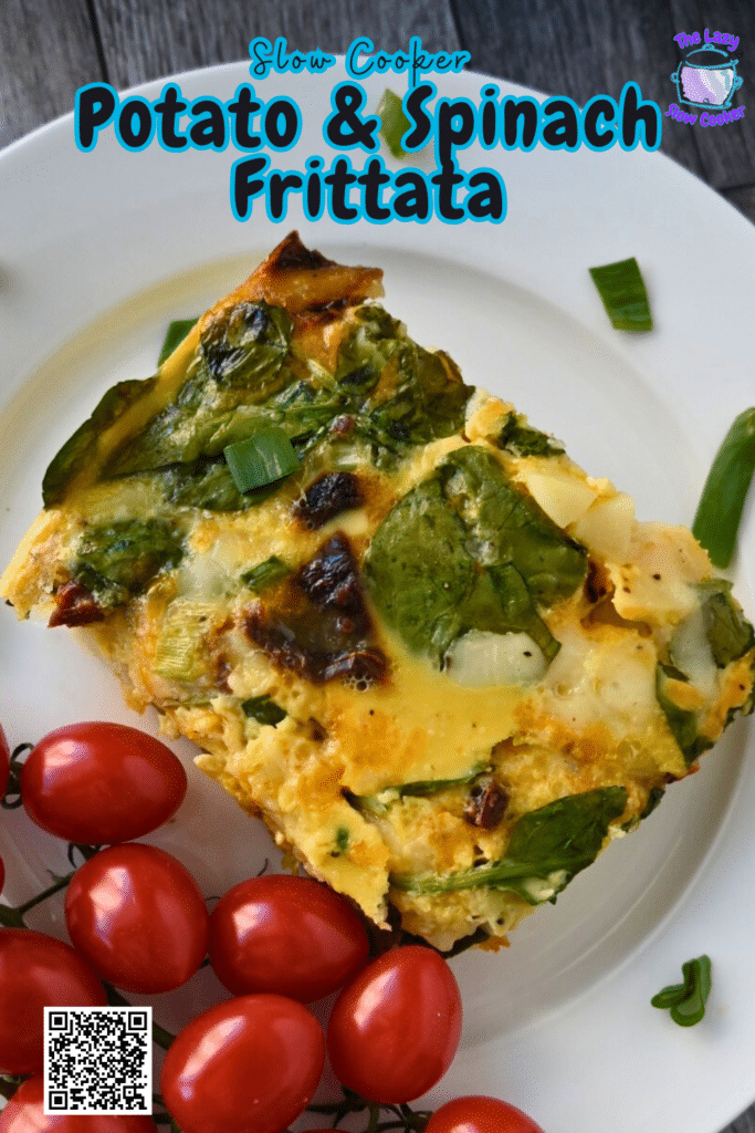 A slice of vegetable frittata with spinach on a white plate, garnished with green onion and served with a bunch of grape tomatoes. The plate is on a rustic wooden surface.