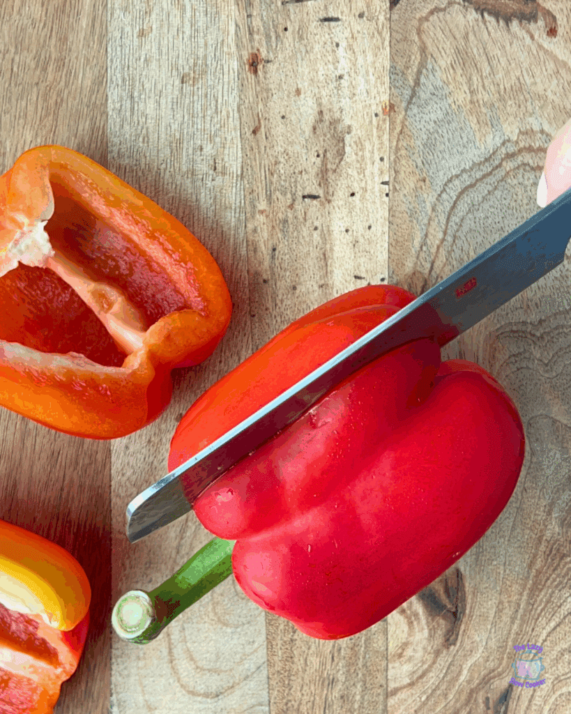 peppers on a cutting board. one is being sliced by a knife