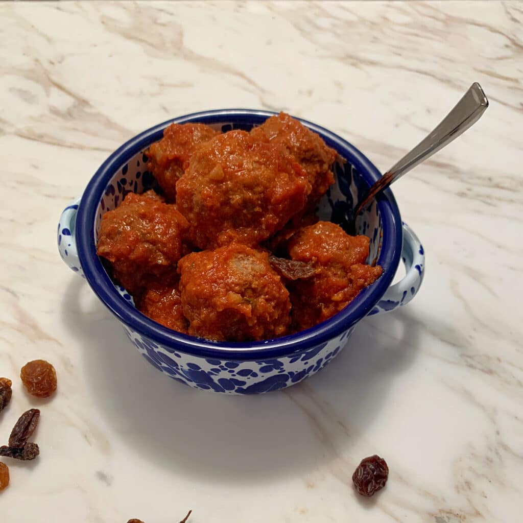 Meatballs in a bowl with a blue rim with a spoon sticking out