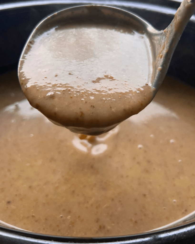 cream of mushroom soup on a ladle held over a crock pot of the same