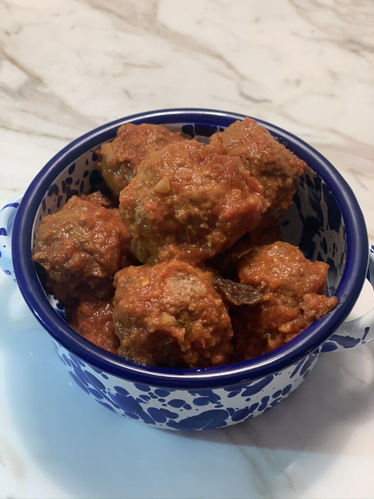 Close up of a round blue and white bowl containing saucy meatballs