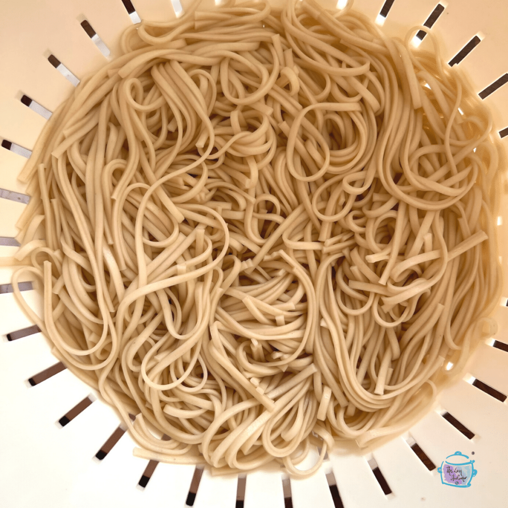 cooked udon noodles in a stainer prior to being added to chicken corn soup