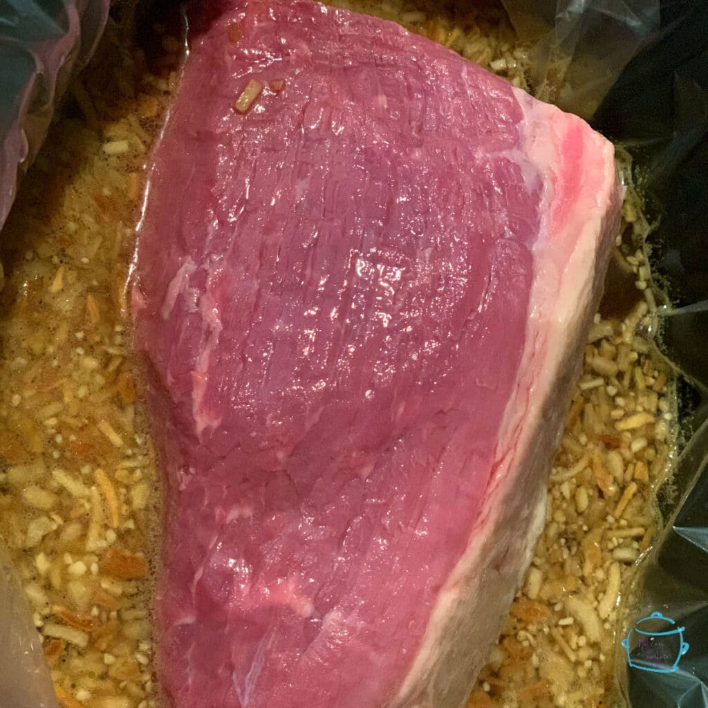 A raw roast sitting in a slow cooker surrounded by liquids and spices