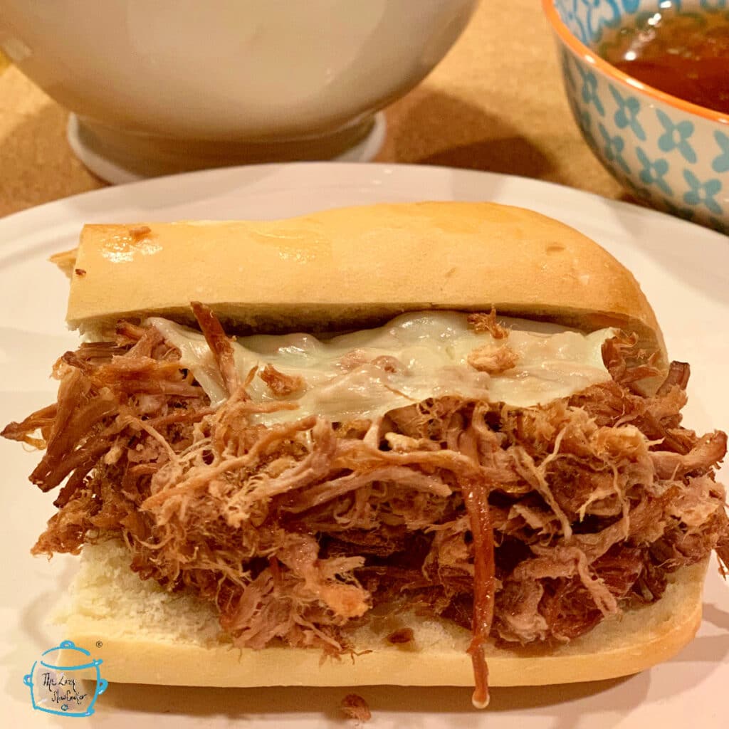 French dip sandwich with melted cheese on a plate with some bowls in the background