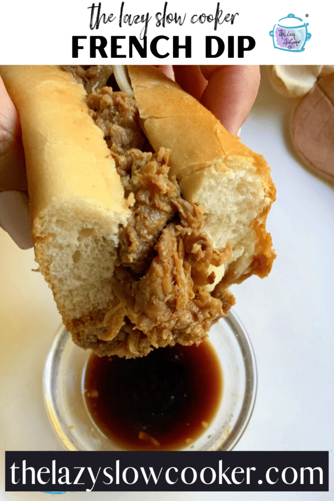 a roll filled with shredded beef held over a small glass bowl filled with au just ready to dip