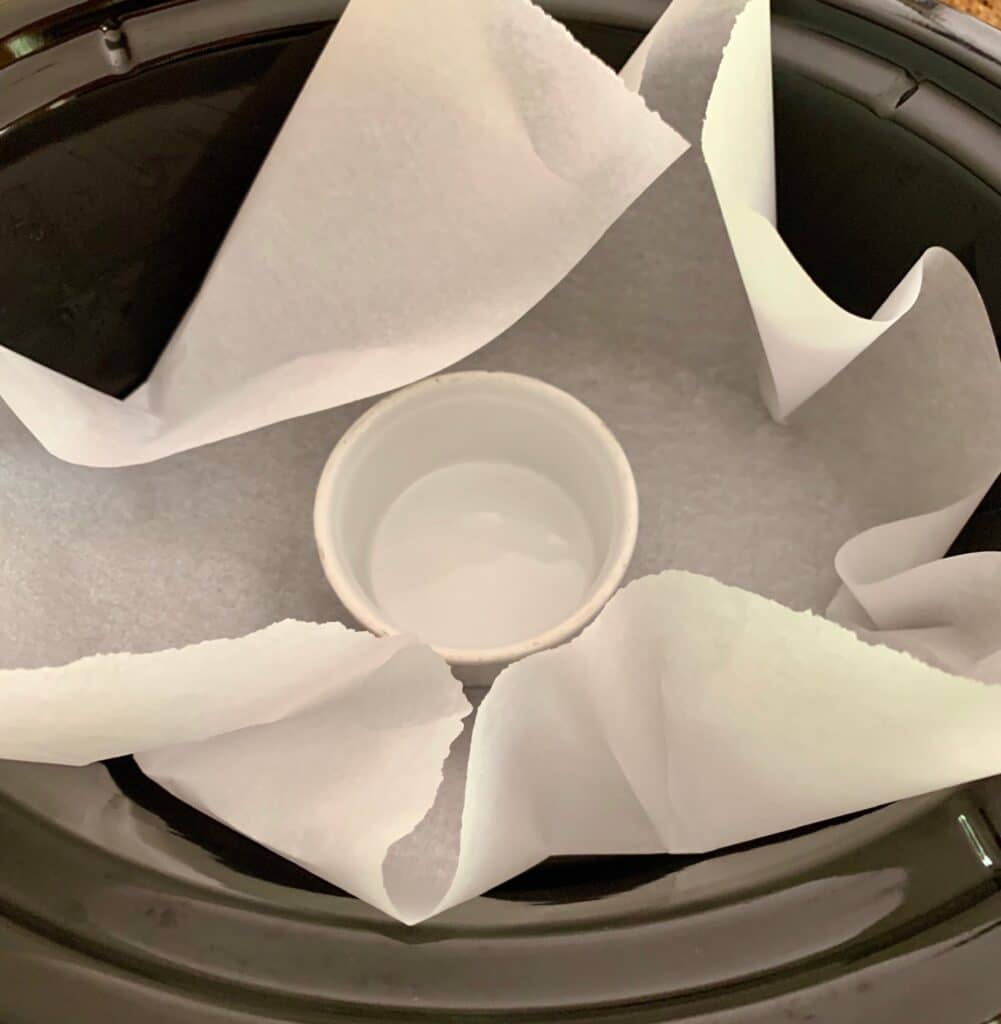 an oval crockpot with parchment paper and a ramekin inside