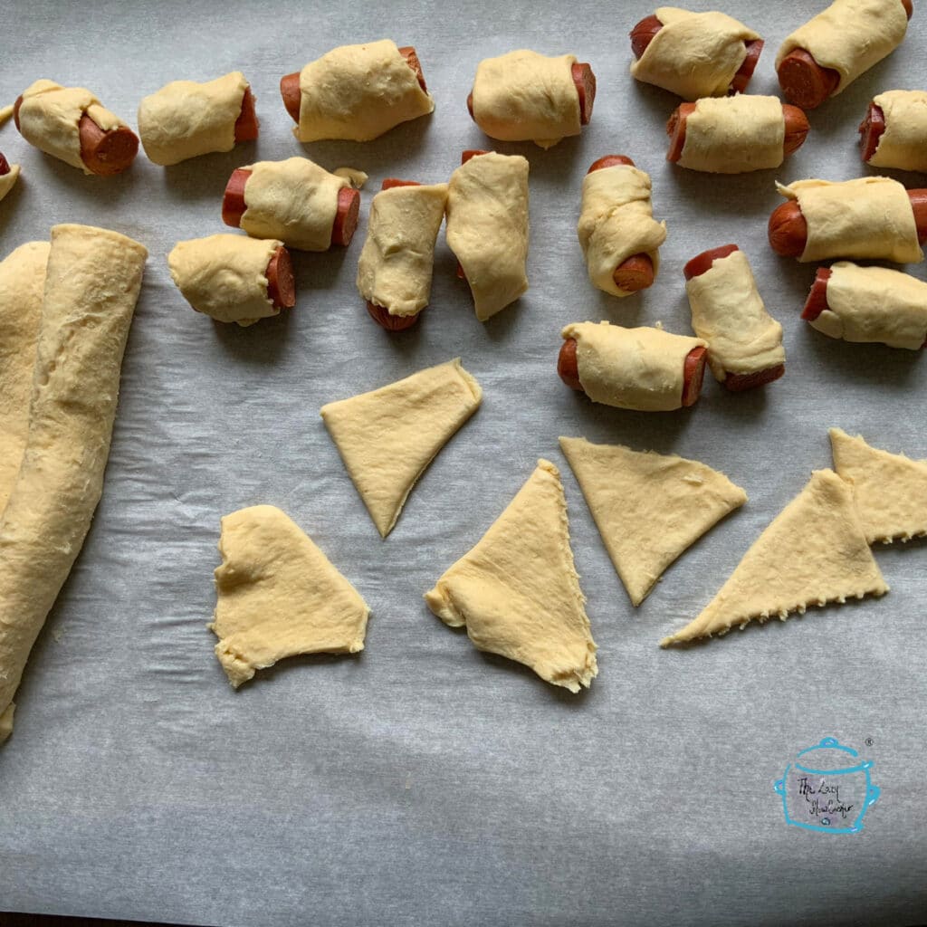 small dogs wrapped in dough next to some dough triangles