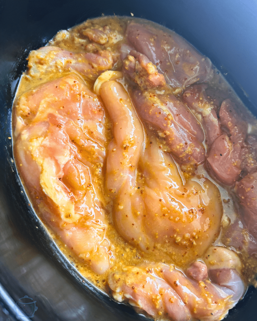chicken in a slow cooker covered in honey mustard sauce before cooking
