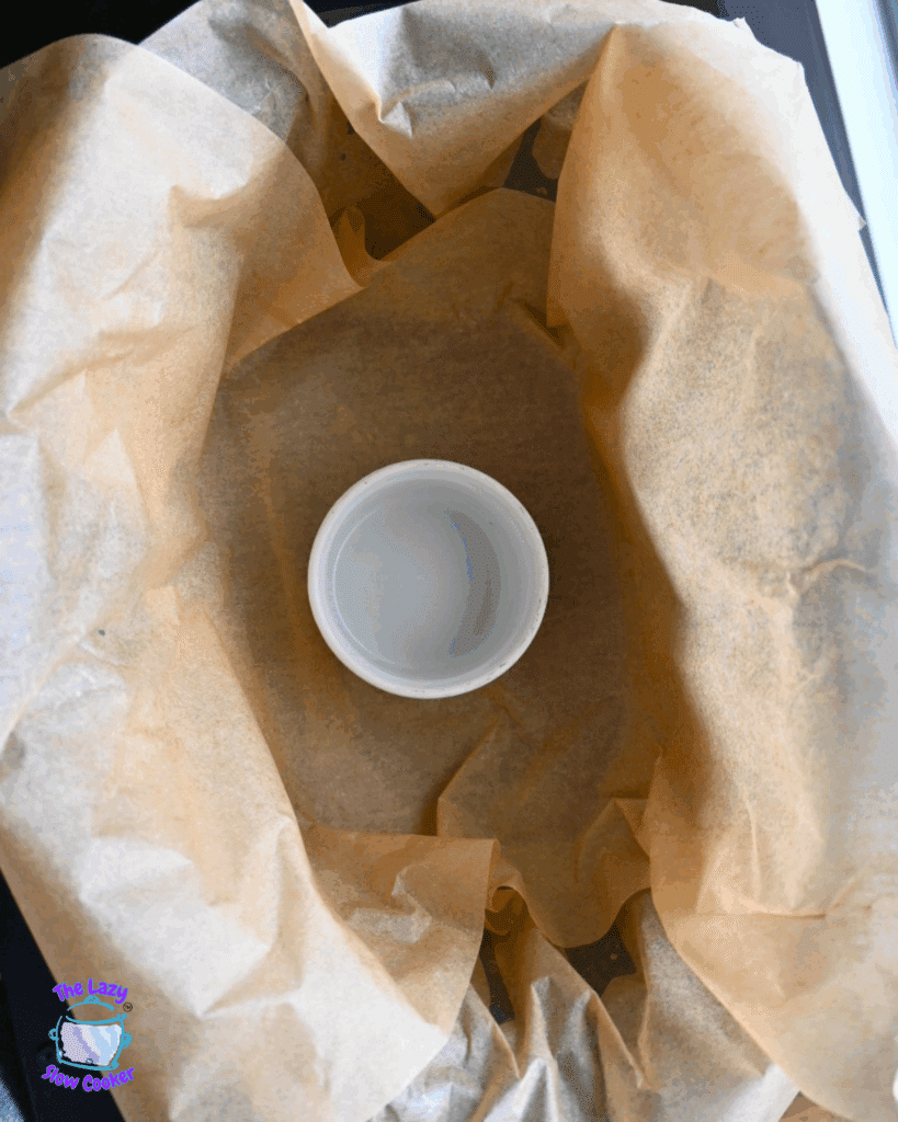 a slow cooker lined with parchment paper with a white ramekin in the middle