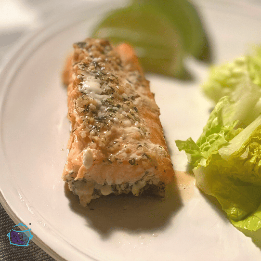 A round white plate with a piece of cooked salmon, lettuce and lime wedges