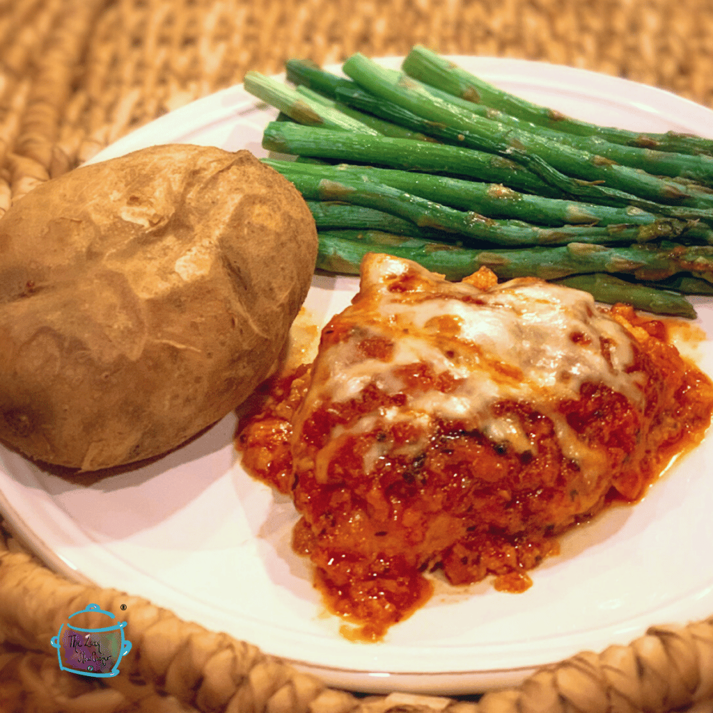 slow cooker chicken parmesan on a plate with a potato and asparagus