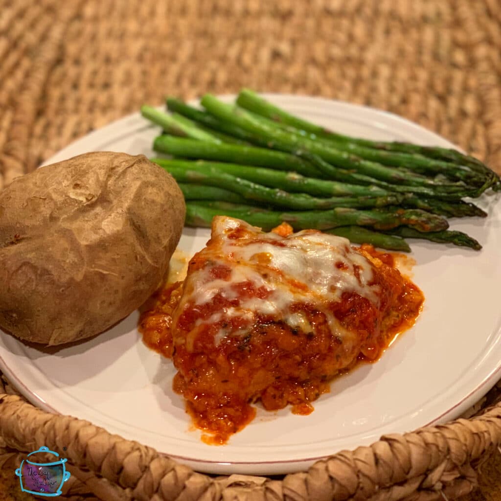 Chicken parmesan on a white plate with potato and asparagus