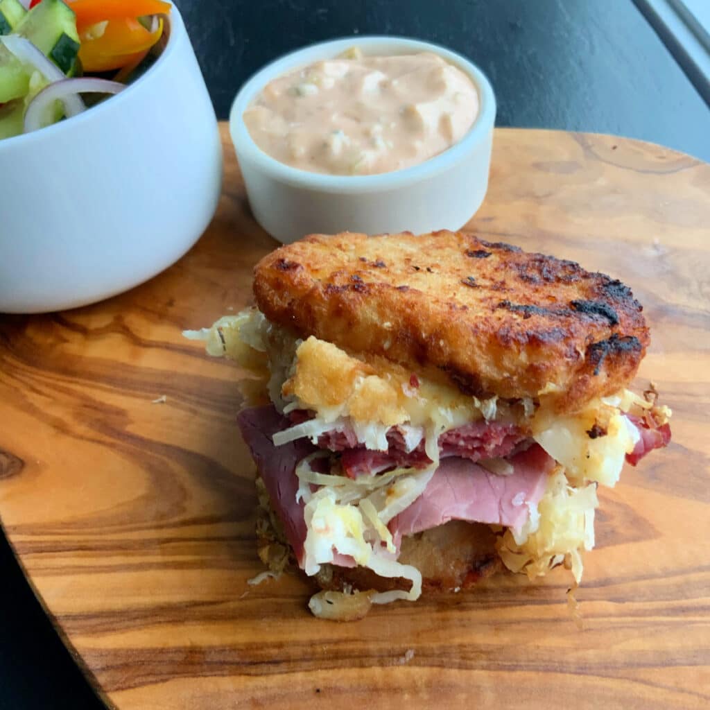 Potato pancake grilled Reuben sandwich on a wooden board with Russian dressing dip in the background