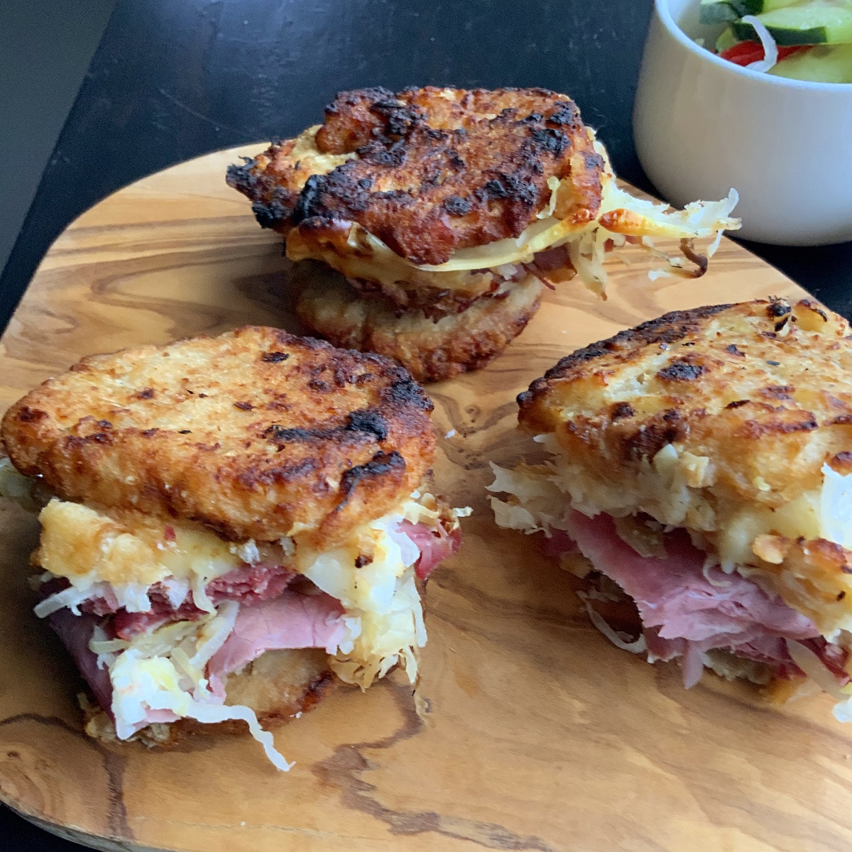 Potato pancake grilled Reuben sandwich on a wooden board with a salad in the background