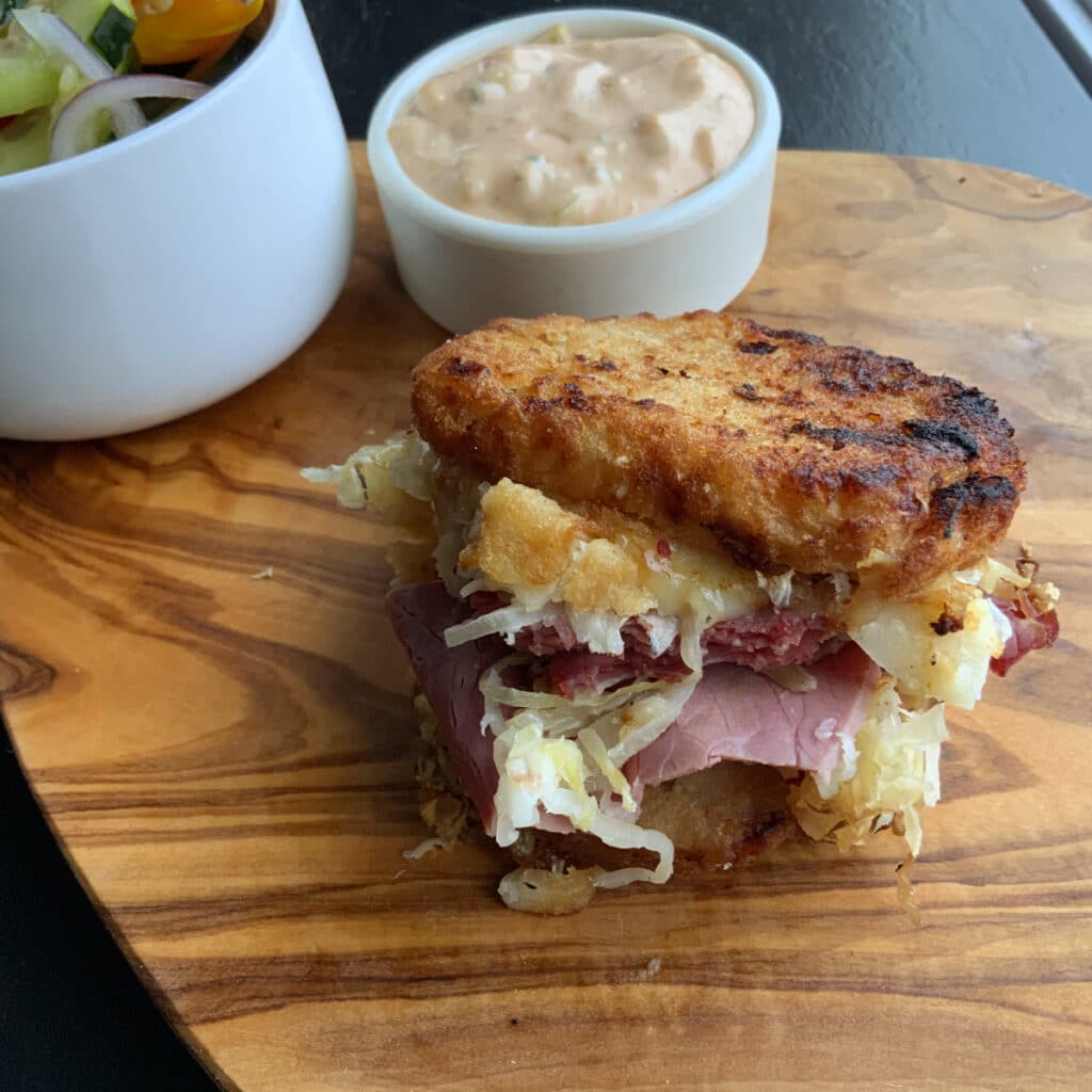 Potato pancake grilled Reuben sandwich on a wooden board with Russian dressing dip in the background