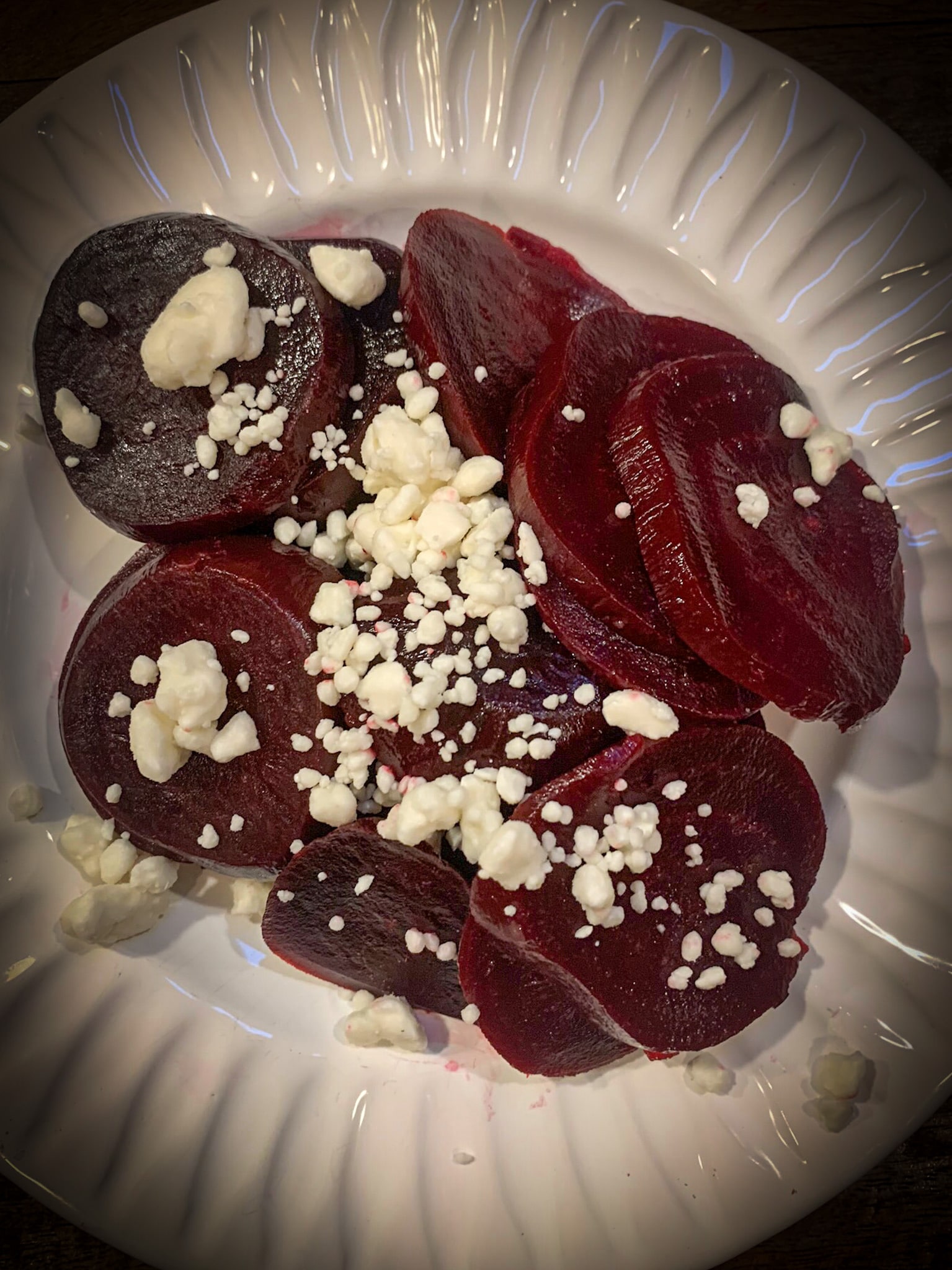 Close up shot of sliced beets with feta cheese crumbles on a white plate.