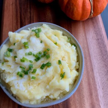 mashed potatoes in a bowl topped with chopped green onions and butter with a pumpkin in the background
