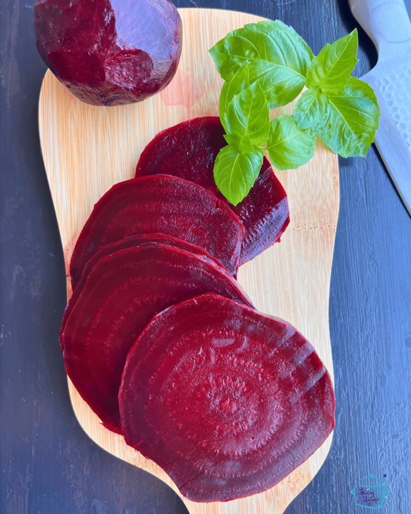 sliced beets on a wooden cutting board with fresh basil