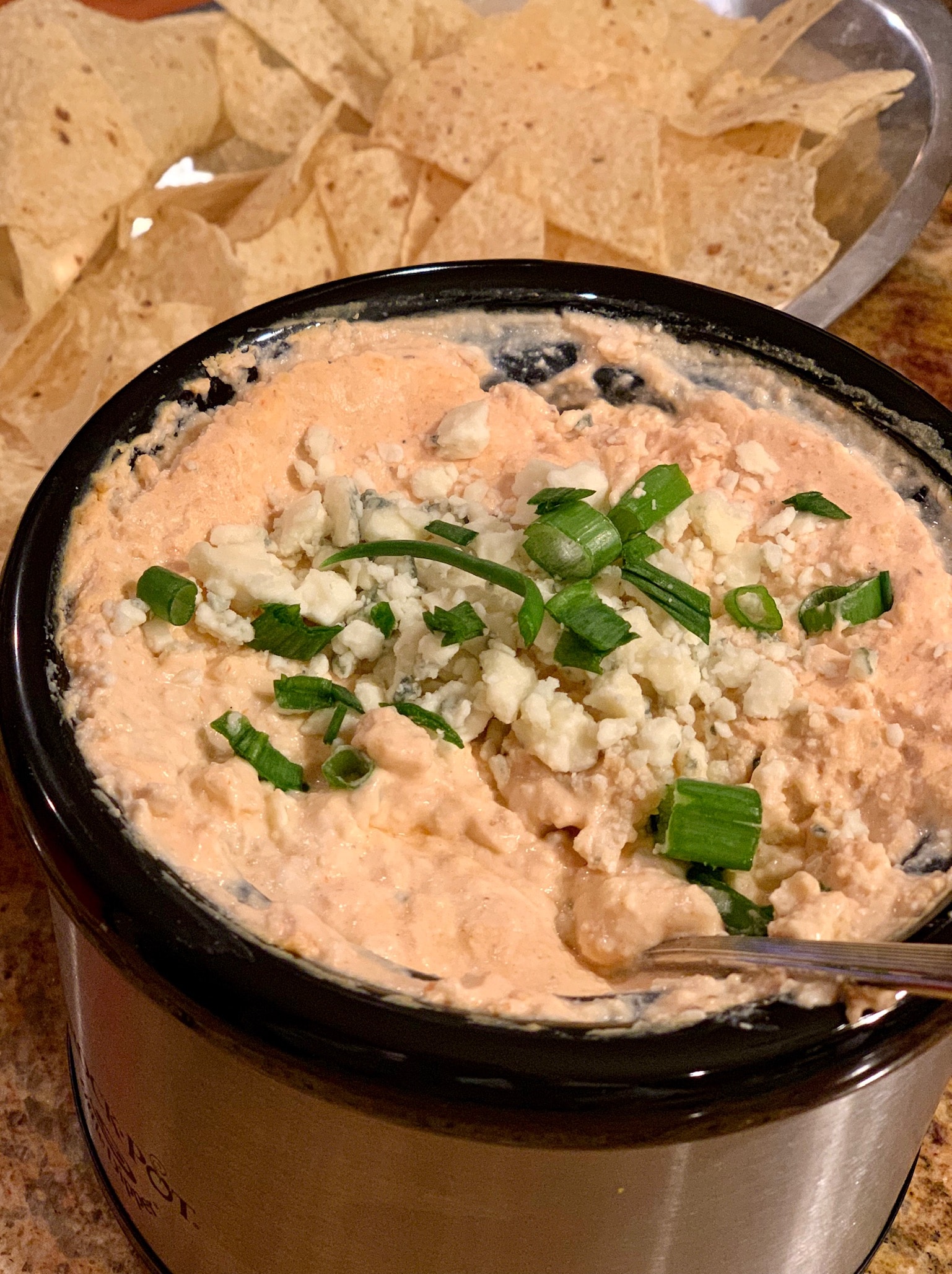 photo of light chicken buffalo dip in small slow cooker topped with blue cheese crumbles and green onion.