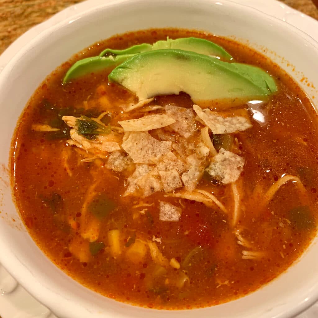 Tortilla soup with wedges of avocado on top and some crumbled tortilla chips
