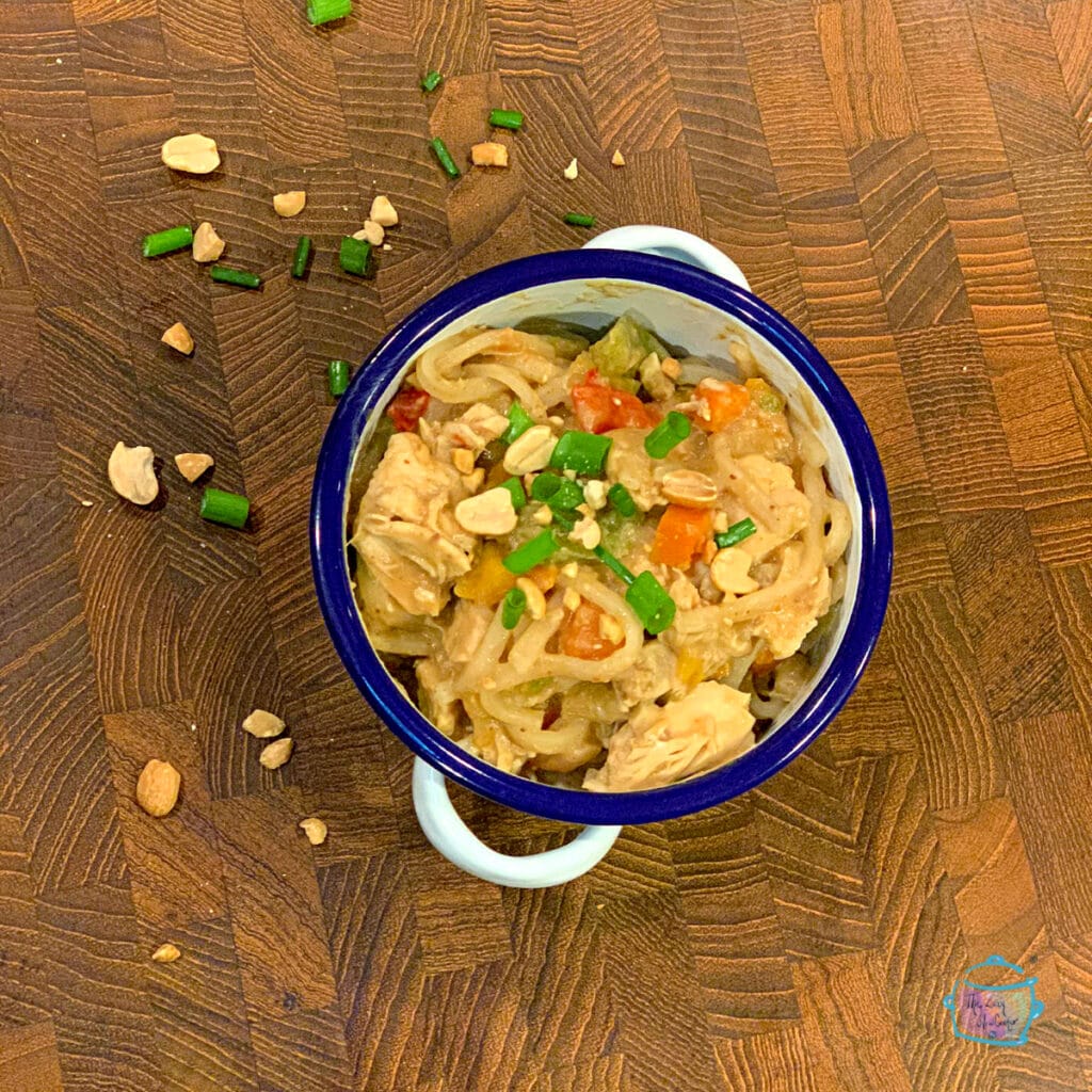 Looking down on a bowl of noodles and chicken topped with peanuts