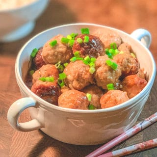 Chicken Teriyaki meatballs in a white bowl with pink chopsticks in foreground
