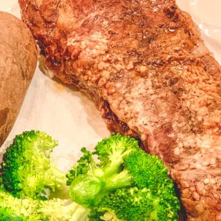 Cooked steak on a white plate served with Broccoli and a potato