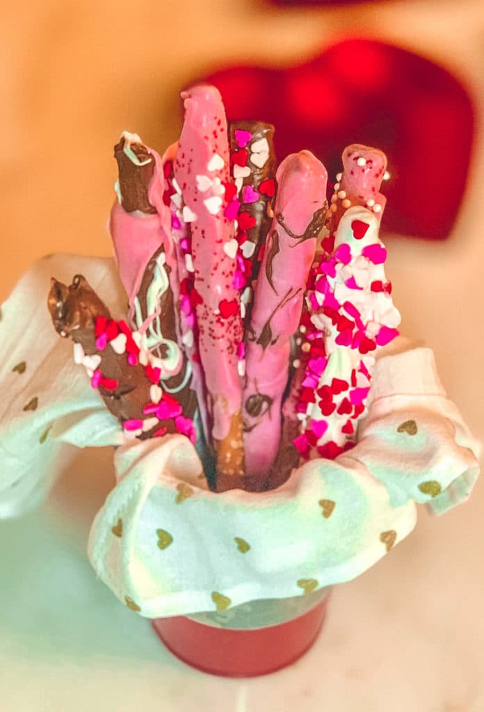 pretzel sticks coated in pink, white and dark chocolate with heart shaped sprinkles