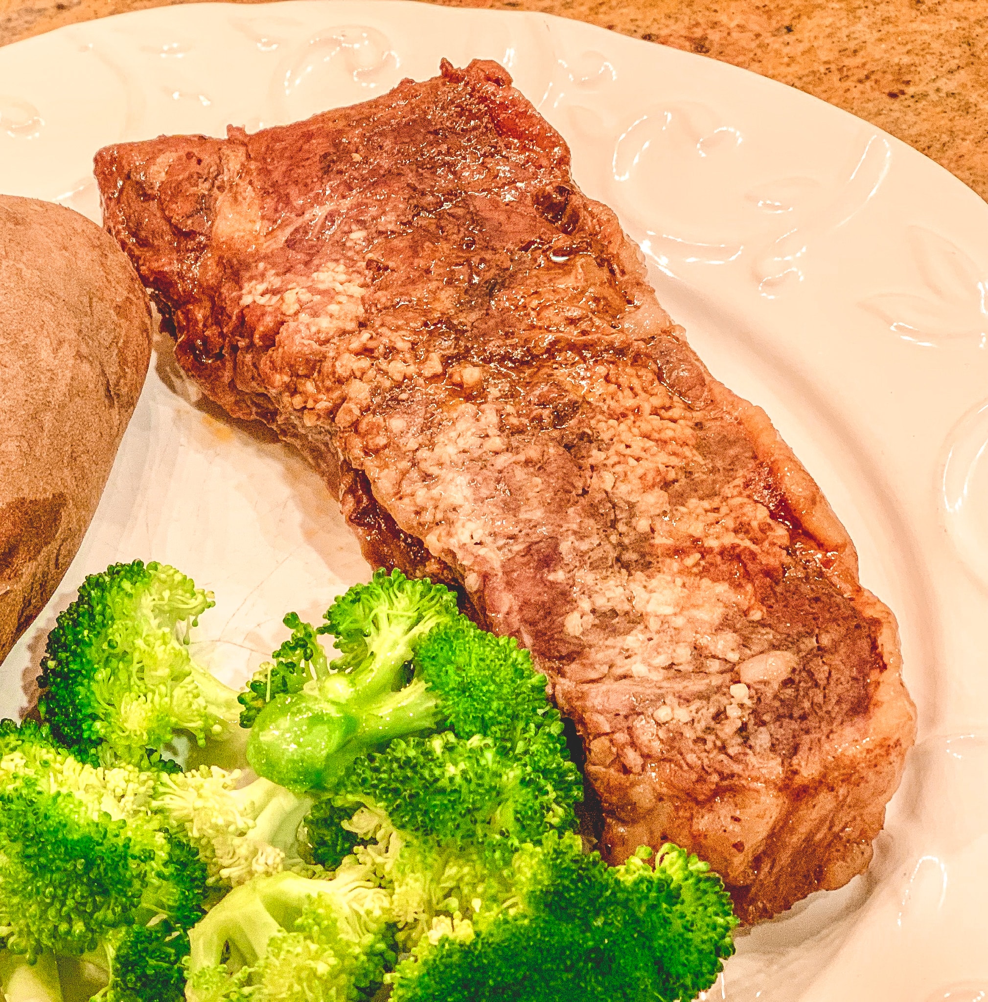 Steak on a white plate with garlic, broccoli.