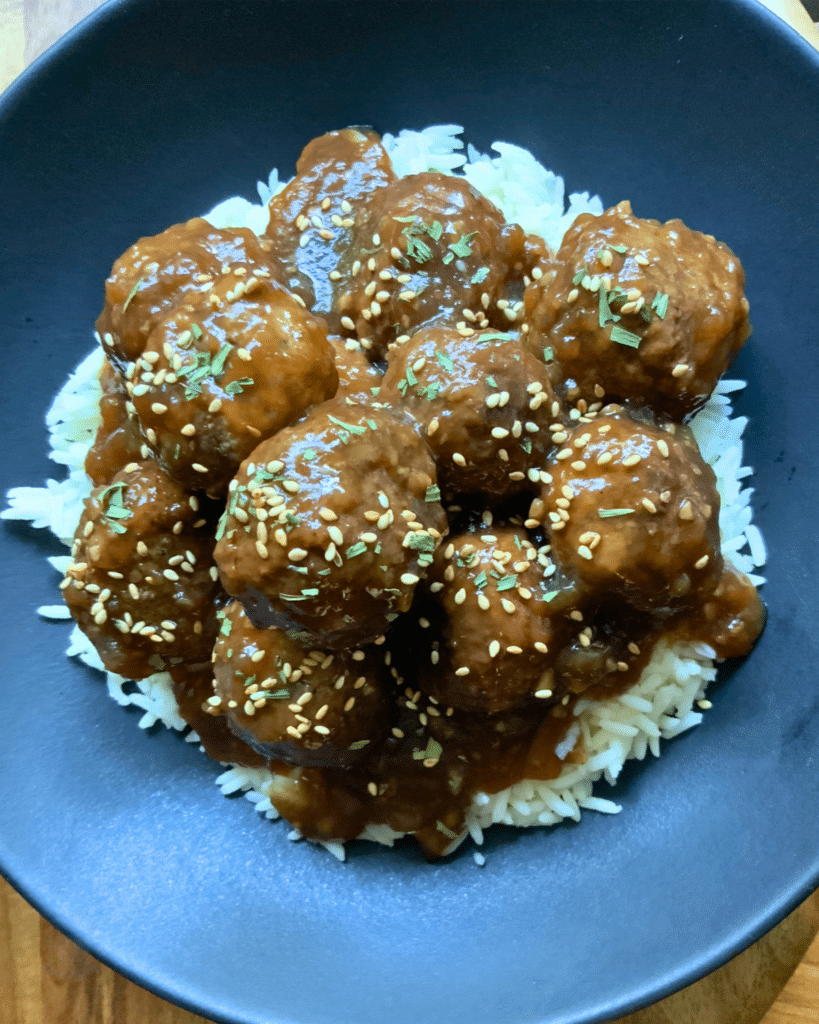 meatballs in a black bowl over rice topped with sesame seeds
