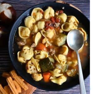 turkey sausage tortellini soup in a black bowl with a spoon