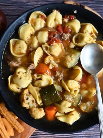 turkey sausage tortellini soup in a black bowl with a spoon