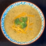 Top down view of bowl of broccoli cheddar soup with fresh broccoli and cheese shreds floating on top