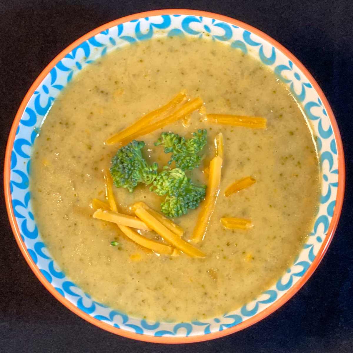 Top down view of bowl of broccoli cheddar soup with fresh broccoli and cheese shreds floating on top
