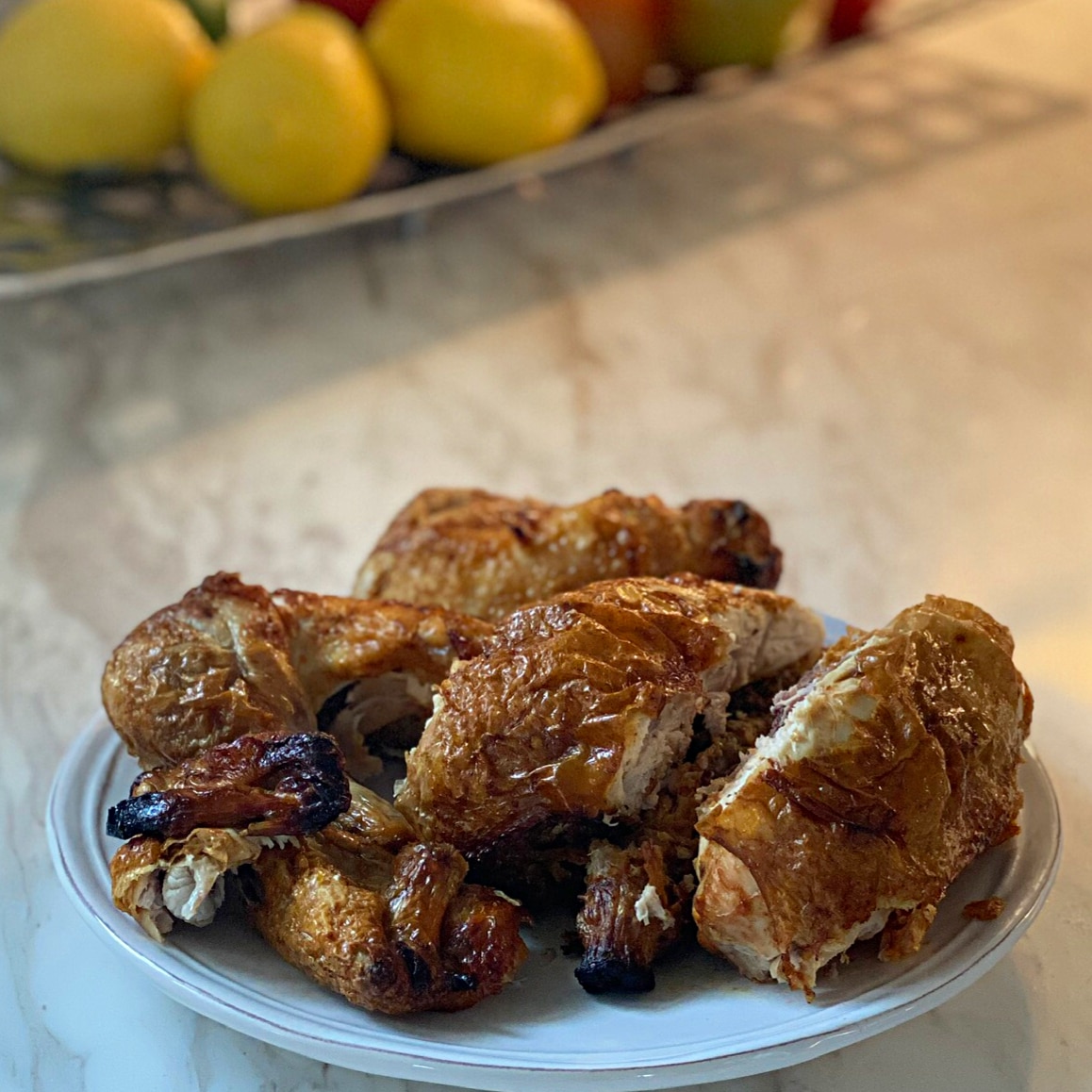 Side view of a whole cut up chicken on a white plate in front of lemons