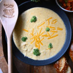 A bowl full of broccoli cheddar slow cooker soup with a wooden spoon
