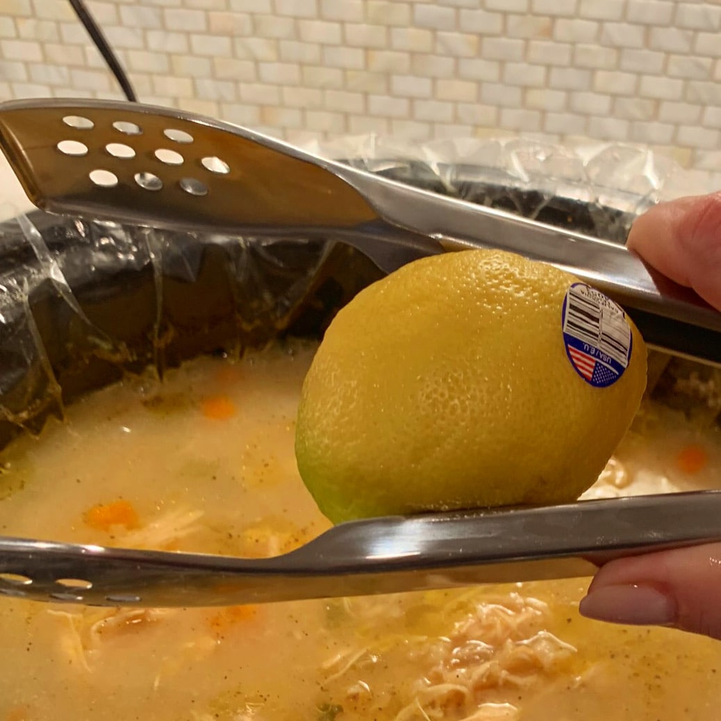 Half a lemon being squeezed over a crockpot with tongs
