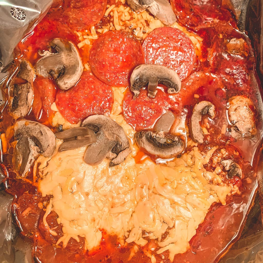 Top view of a crockpot filled with chicken, sauce, shredded cheese, pepperoni and mushrooms