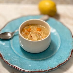 Side view of a white round bowl filled with soup with a lemon in the background