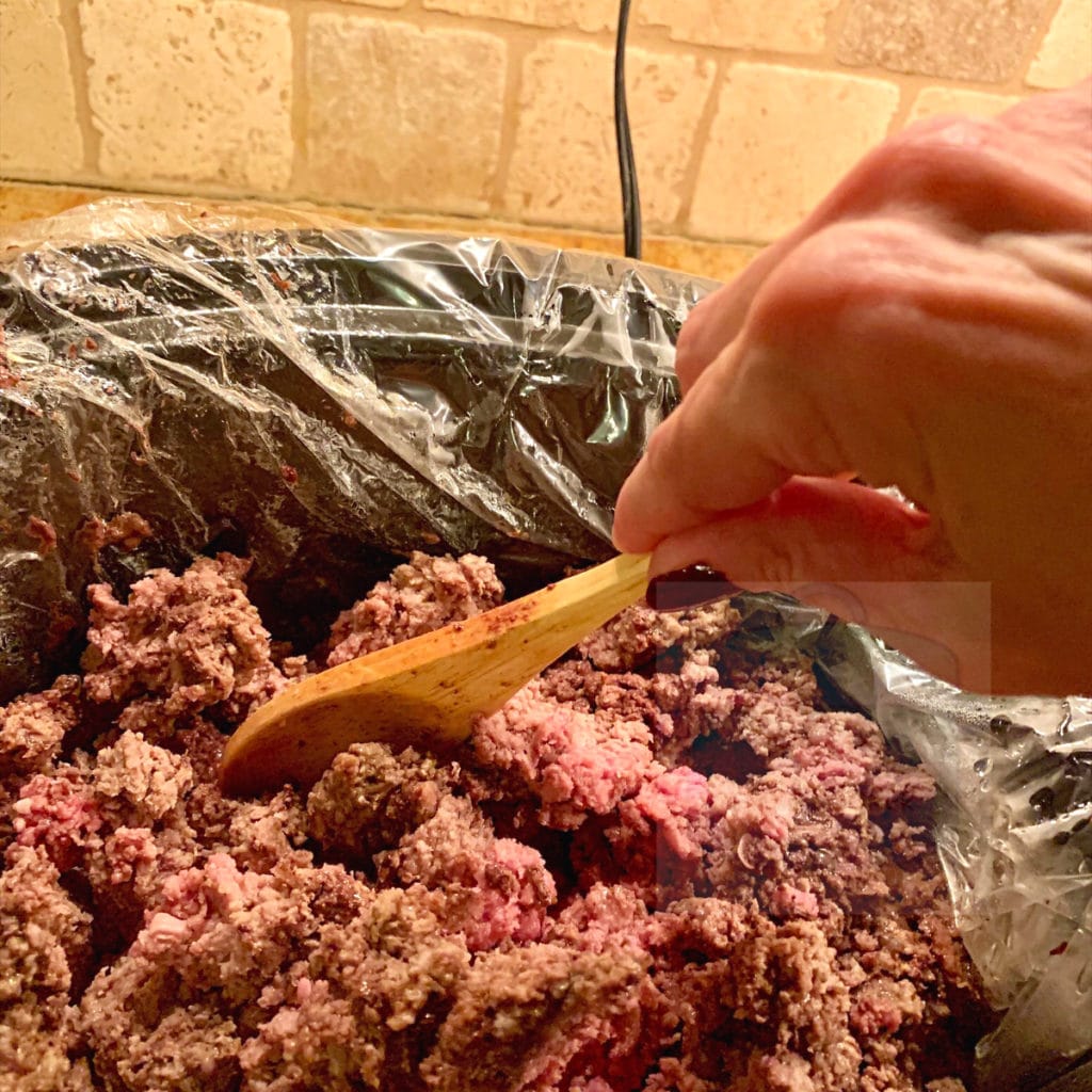 View of browning ground beef with slow cooker stirring with a wooden spoon