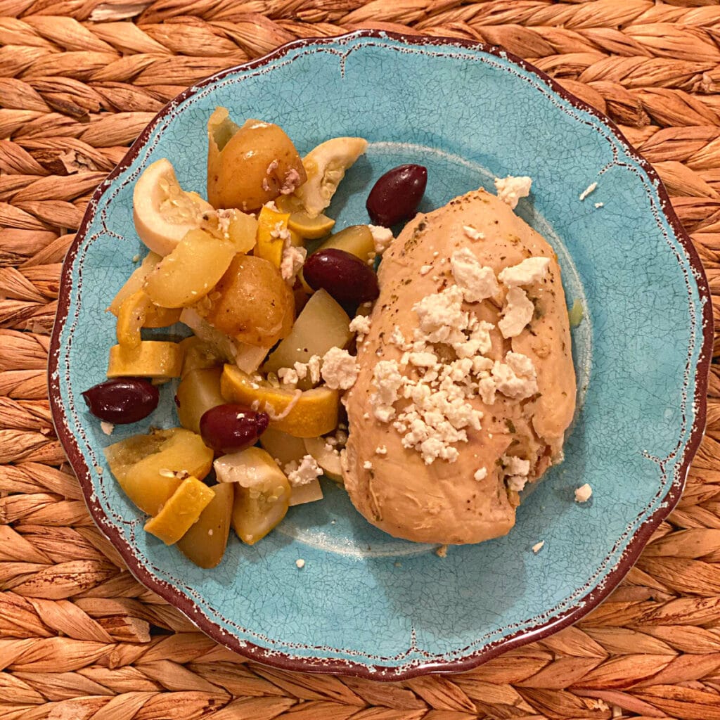 top view of a cooked chicken breast topped with feta cheese, kalamata olive and greek veggies