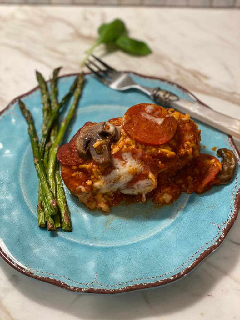 slow cooker pizza chicken on a blue plate with asparagus