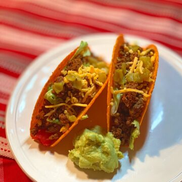 Photo of two hard shelled tacos filled with ground beef, green chili peppers and shredded cheese
