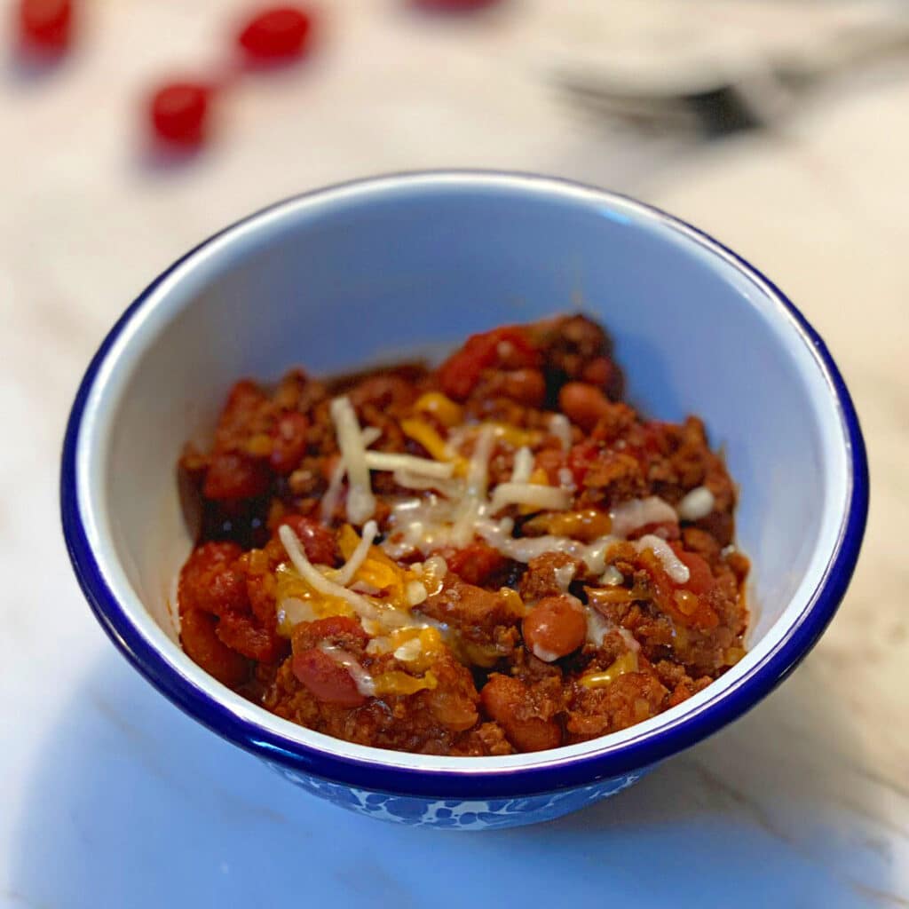 white bowl with blue trim filled with chili with a little melted cheese on top